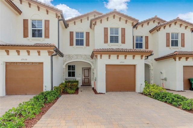 mediterranean / spanish-style home featuring a garage, stucco siding, a tiled roof, and decorative driveway
