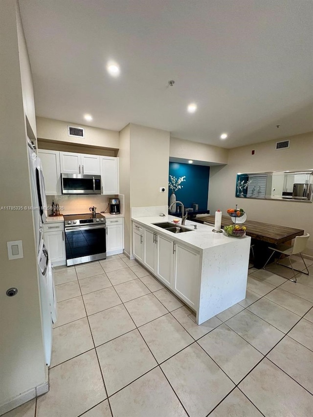 kitchen with a peninsula, appliances with stainless steel finishes, light tile patterned floors, and a sink
