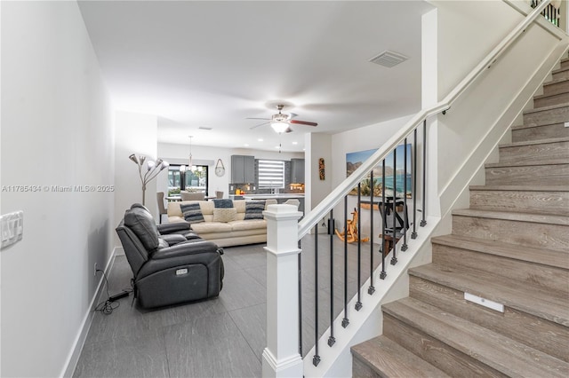 living area featuring visible vents, baseboards, a ceiling fan, and stairs