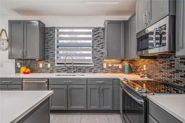 kitchen featuring gray cabinetry, a sink, decorative backsplash, light countertops, and appliances with stainless steel finishes