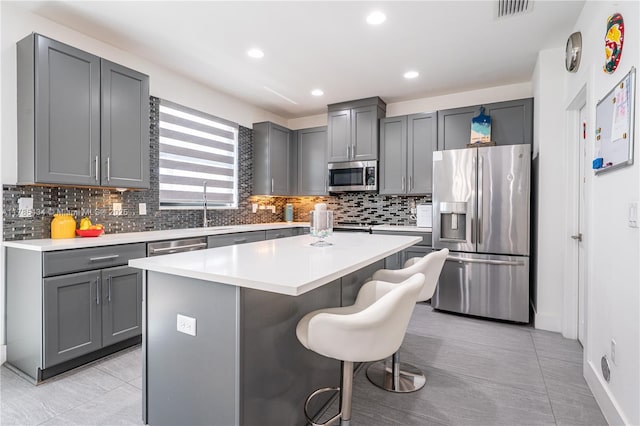 kitchen featuring stainless steel appliances, gray cabinets, visible vents, a kitchen island, and tasteful backsplash