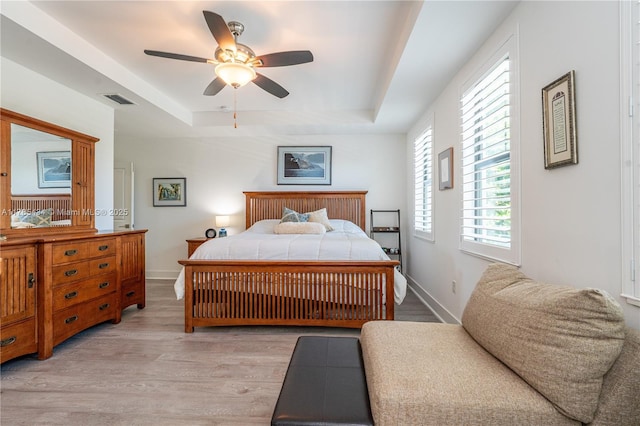 bedroom with visible vents, light wood finished floors, a ceiling fan, a tray ceiling, and baseboards