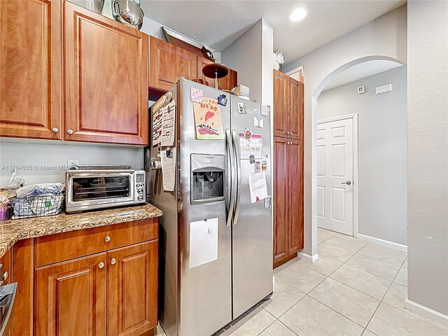 294 Las Brisas Cir, Sunrise, FL 33326 - kitchen featuring stainless steel refrigerator with ice dispenser, arched walkways, light tile patterned floors, brown cabinetry, and light stone counters