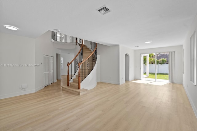 unfurnished living room featuring arched walkways, stairs, baseboards, light wood-type flooring, and visible vents