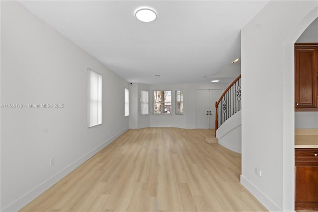 unfurnished living room featuring baseboards, light wood-style flooring, and stairway