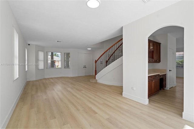 unfurnished living room with visible vents, stairs, baseboards, arched walkways, and light wood finished floors