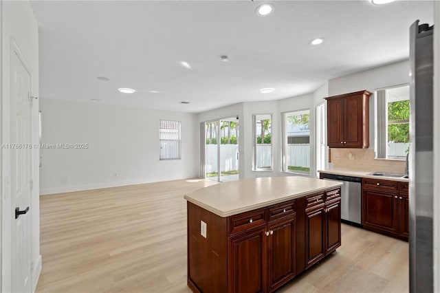 kitchen featuring dishwasher, light countertops, light wood-style flooring, a center island, and tasteful backsplash