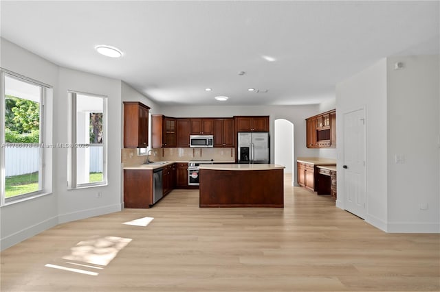 kitchen featuring a sink, light wood finished floors, arched walkways, stainless steel appliances, and baseboards