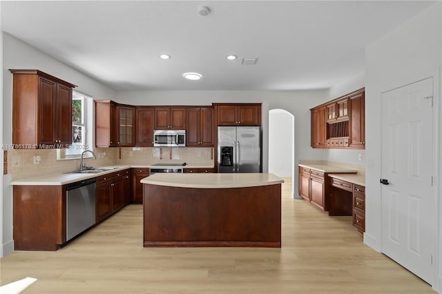 kitchen with stainless steel appliances, arched walkways, a sink, and light wood-type flooring
