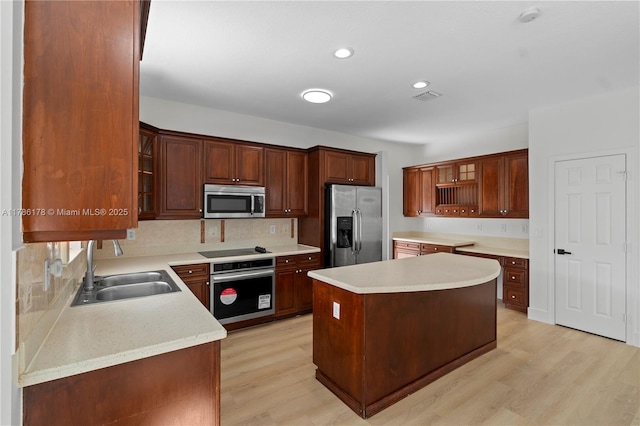 kitchen with stainless steel appliances, decorative backsplash, a sink, and light wood finished floors