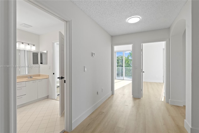 hall featuring light wood-style floors, a sink, a textured ceiling, and baseboards