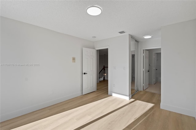 unfurnished bedroom with a textured ceiling, baseboards, visible vents, and wood finished floors