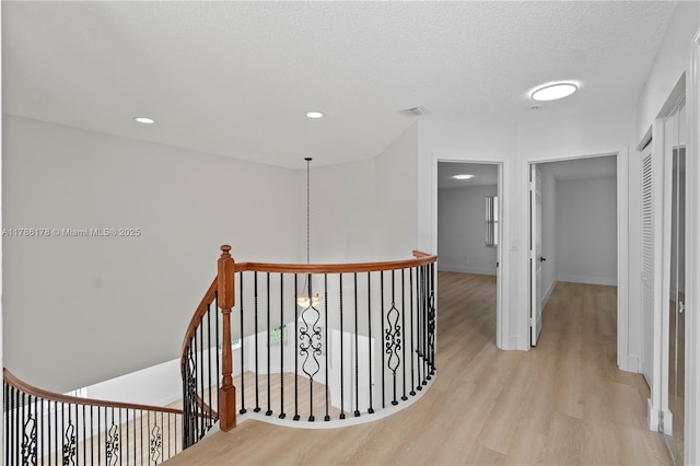 corridor with visible vents, light wood-style flooring, baseboards, and an upstairs landing