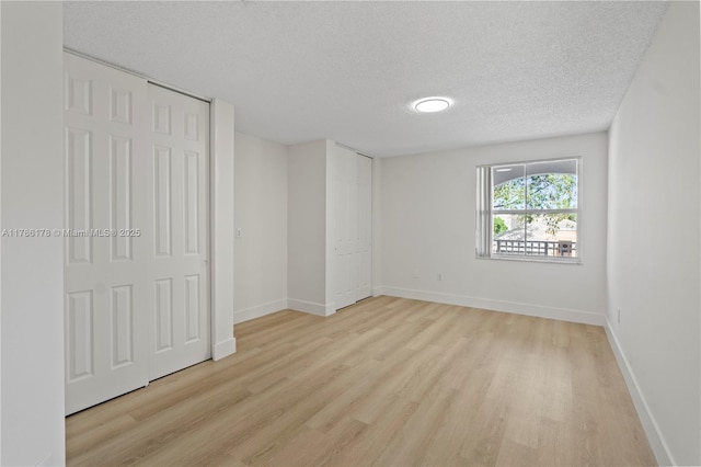 unfurnished bedroom featuring baseboards, a textured ceiling, and light wood-style flooring
