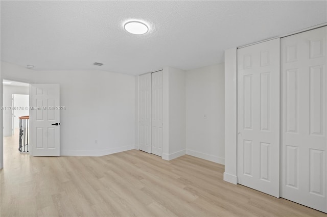 unfurnished bedroom with light wood-style floors, a textured ceiling, baseboards, and visible vents