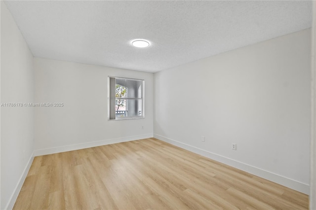 spare room with baseboards, a textured ceiling, and light wood-style flooring