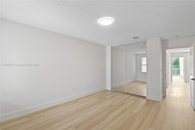 unfurnished bedroom featuring a textured ceiling, light wood-style flooring, baseboards, visible vents, and a closet