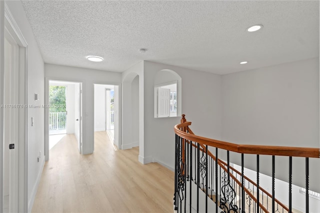 hallway with a textured ceiling, light wood-type flooring, baseboards, an upstairs landing, and recessed lighting