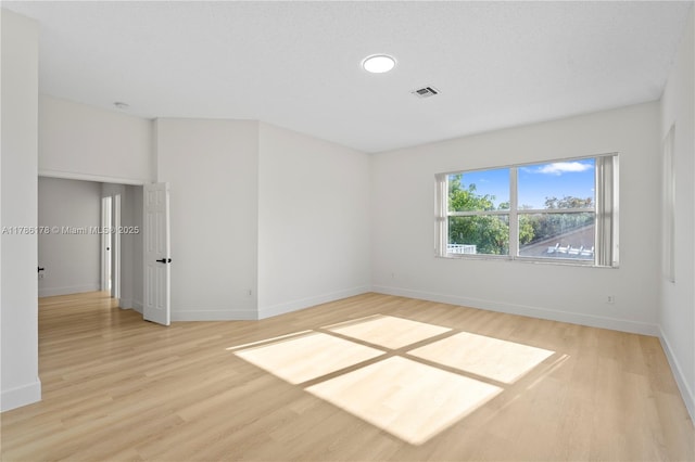 empty room with baseboards, light wood finished floors, and visible vents