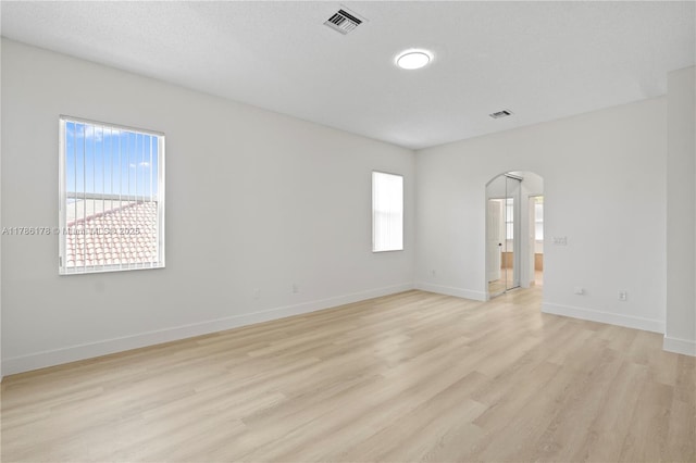 empty room featuring arched walkways, visible vents, a wealth of natural light, and light wood finished floors