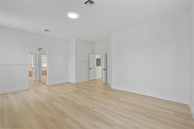 spare room with arched walkways, baseboards, light wood-type flooring, and visible vents