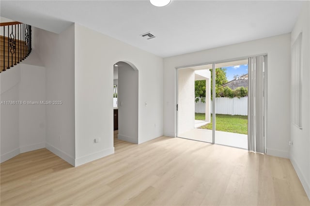 empty room with arched walkways, visible vents, a healthy amount of sunlight, and light wood finished floors