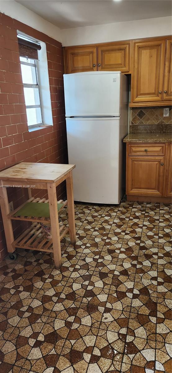 kitchen with decorative backsplash, freestanding refrigerator, and brown cabinets
