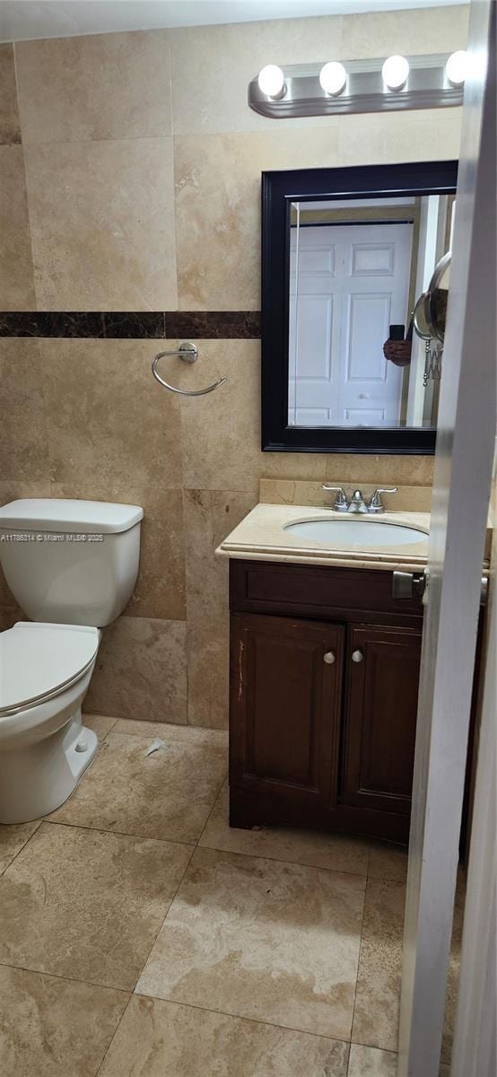 half bathroom featuring tile walls, toilet, and vanity