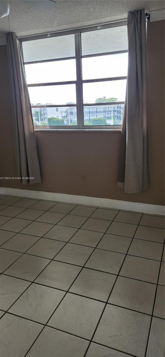 unfurnished room featuring plenty of natural light, baseboards, a textured ceiling, and light tile patterned floors