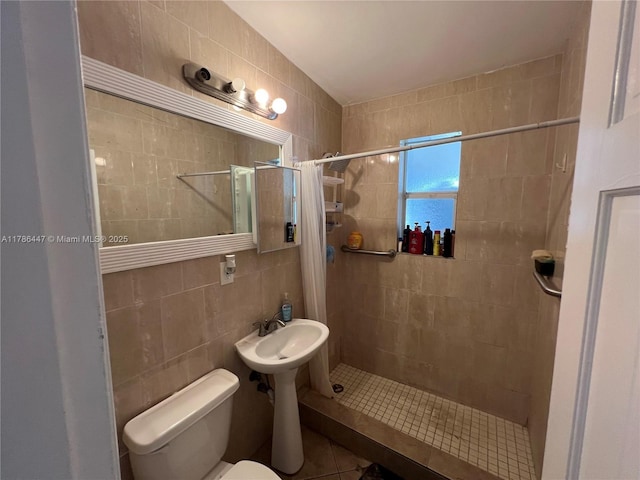 bathroom with tile walls, toilet, tiled shower, and tile patterned floors