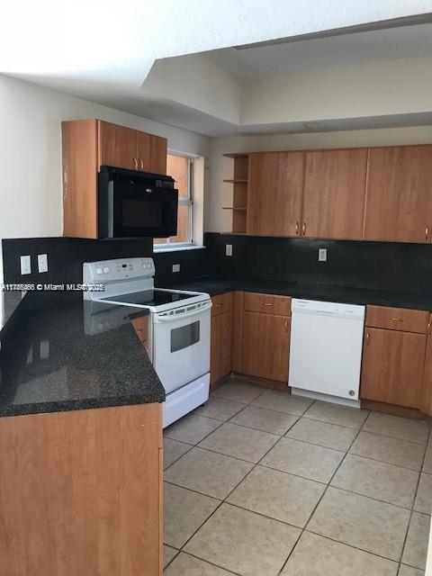 948 SW 6th Ct, Florida City, FL 33034 - kitchen with a tray ceiling, light tile patterned flooring, white appliances, open shelves, and brown cabinetry