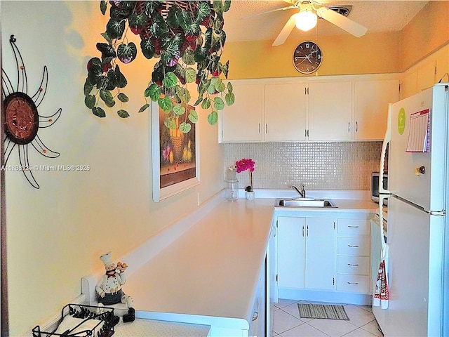 kitchen featuring freestanding refrigerator, a ceiling fan, light countertops, tasteful backsplash, and a sink