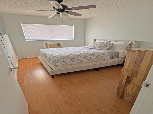 bedroom with an AC wall unit, a textured ceiling, ceiling fan, and wood finished floors