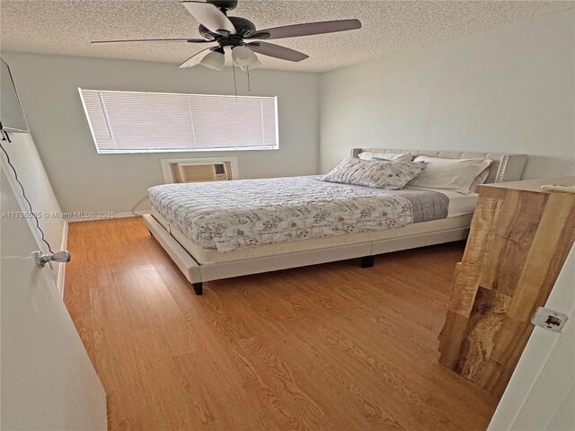 bedroom with a ceiling fan, a textured ceiling, a wall mounted AC, and wood finished floors