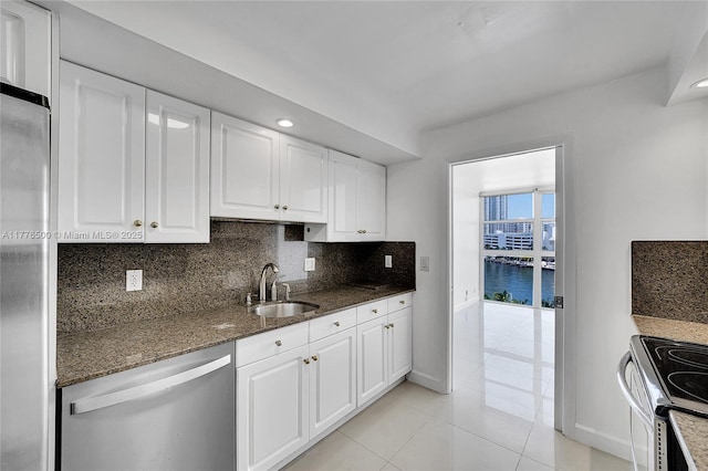 kitchen with a sink, stainless steel appliances, baseboards, dark stone counters, and white cabinetry