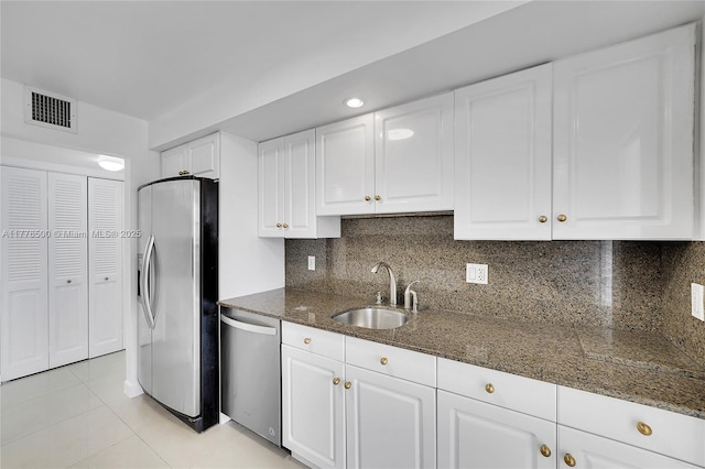 kitchen with stainless steel appliances, a sink, white cabinets, and dark stone counters