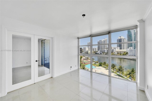 unfurnished room featuring expansive windows, a city view, baseboards, french doors, and a water view