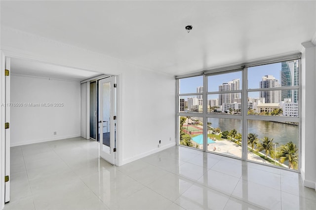 empty room featuring light tile patterned flooring, a city view, baseboards, floor to ceiling windows, and a water view