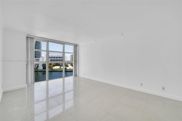 unfurnished room featuring baseboards, expansive windows, a water view, and light tile patterned floors
