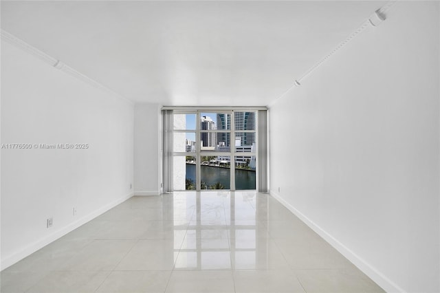 unfurnished room with baseboards, crown molding, expansive windows, light tile patterned floors, and a water view