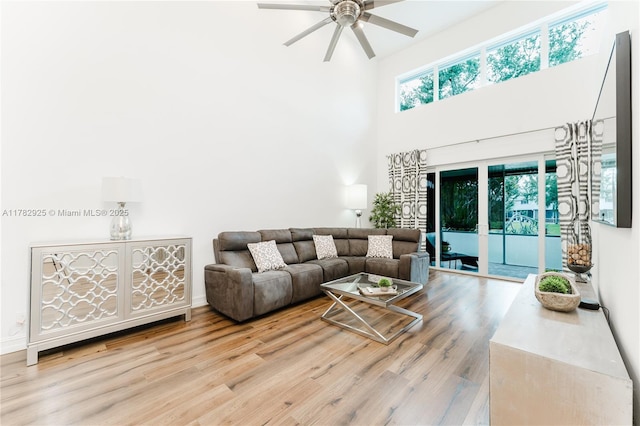 living room with a towering ceiling, a ceiling fan, and wood finished floors