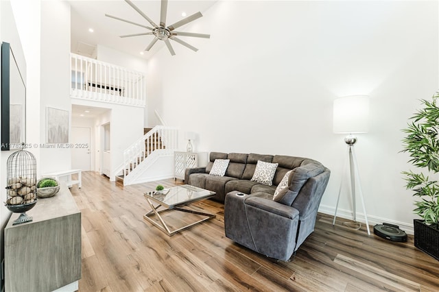 living area featuring baseboards, a ceiling fan, wood finished floors, a high ceiling, and stairs