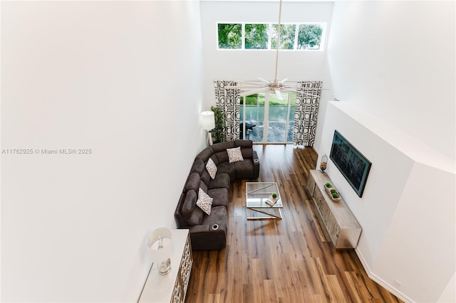 living area featuring wood finished floors, a towering ceiling, a fireplace with raised hearth, and ceiling fan