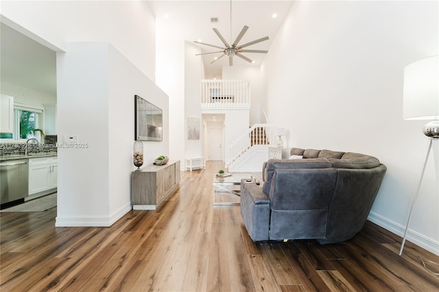 living room featuring a high ceiling, a ceiling fan, wood finished floors, and baseboards