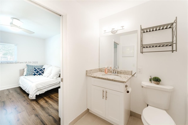 bathroom with wood finished floors, toilet, vanity, a ceiling fan, and baseboards