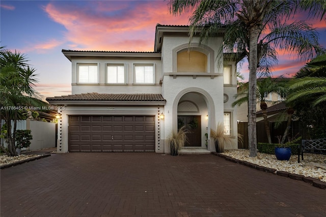 mediterranean / spanish house featuring fence, stucco siding, an attached garage, a tile roof, and decorative driveway