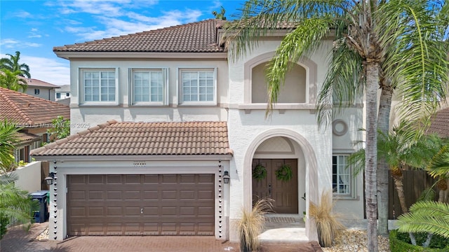mediterranean / spanish-style home featuring stucco siding, decorative driveway, a tiled roof, and a garage