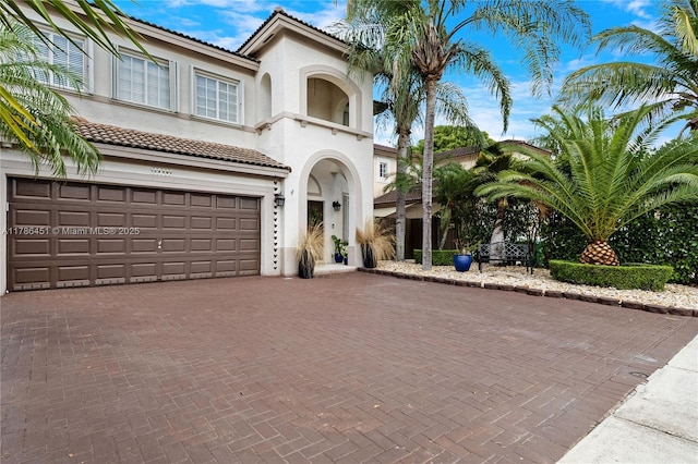 mediterranean / spanish-style house featuring a garage, stucco siding, a tile roof, and decorative driveway