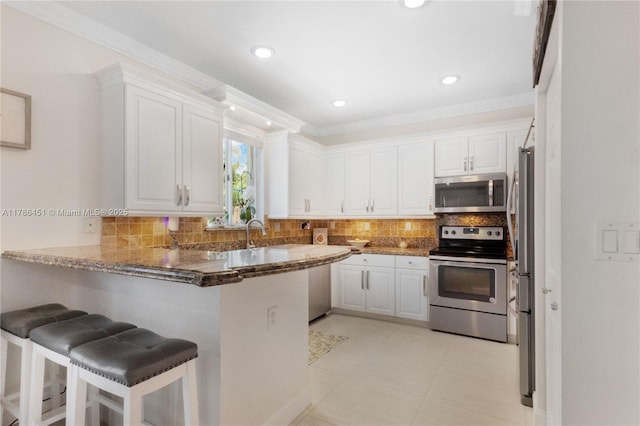 kitchen featuring a peninsula, appliances with stainless steel finishes, dark stone countertops, and crown molding