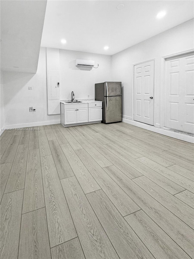 interior space with an AC wall unit, a sink, freestanding refrigerator, light wood-style flooring, and white cabinetry